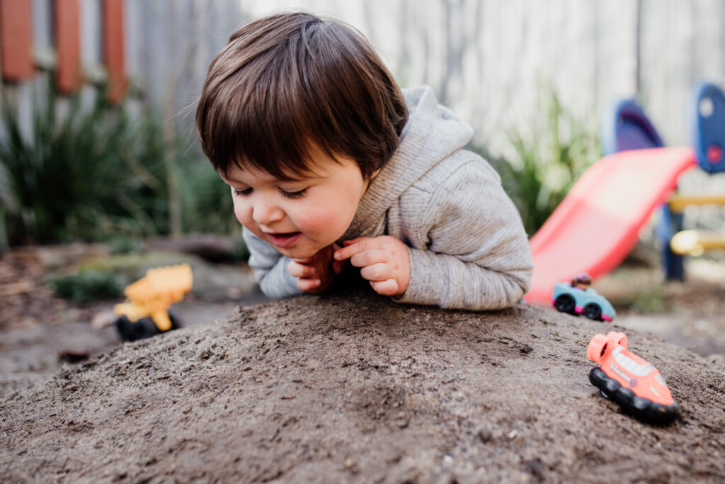 Boy playing with toy cars on mound of dirt